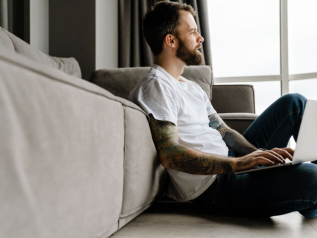 Bearded european man working with laptop while sitting on floor