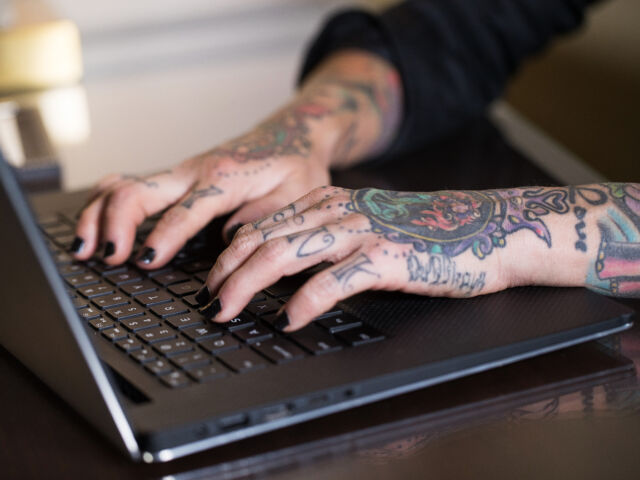 Tattoo hands typing on a laptop computer